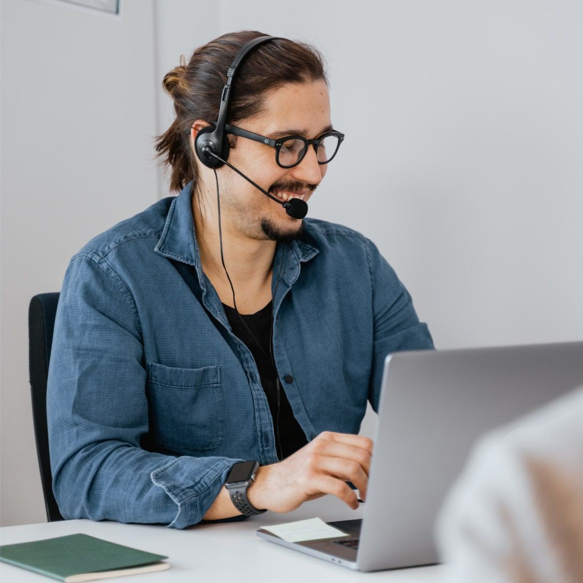 Férfi munkatárs fejhallgatóval a fején laptop előtt telefonál